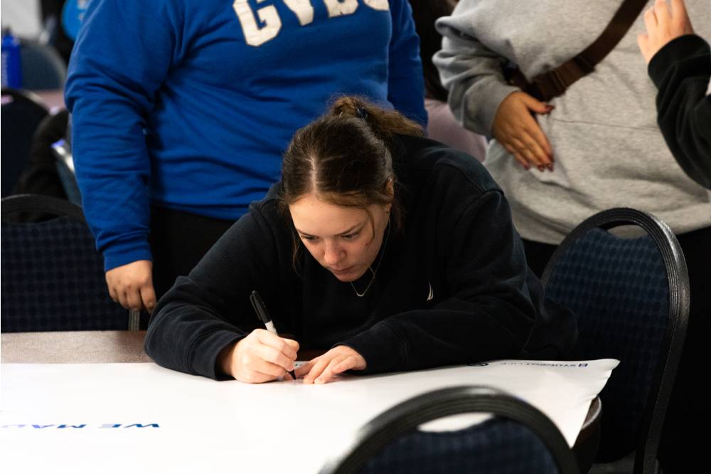A student uses a sharpie to write on a big white banner